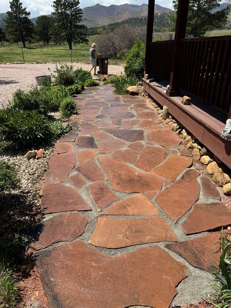 Flagstone path leading to a porch, surrounded by greenery and mountains in the background.
