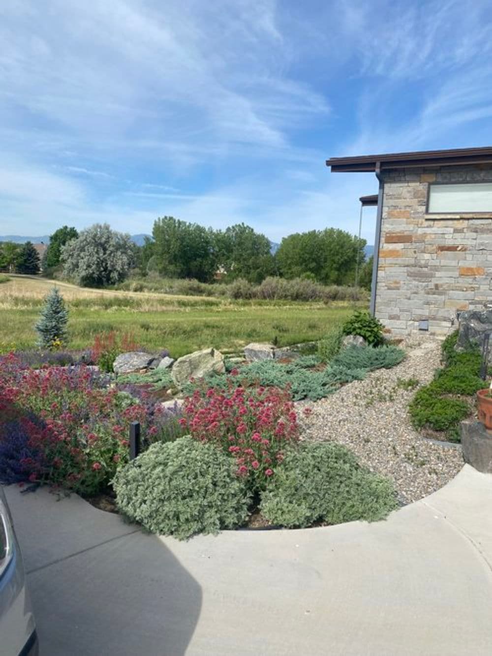 Lush garden with colorful flowers and stone pathway by a modern home in a scenic landscape.