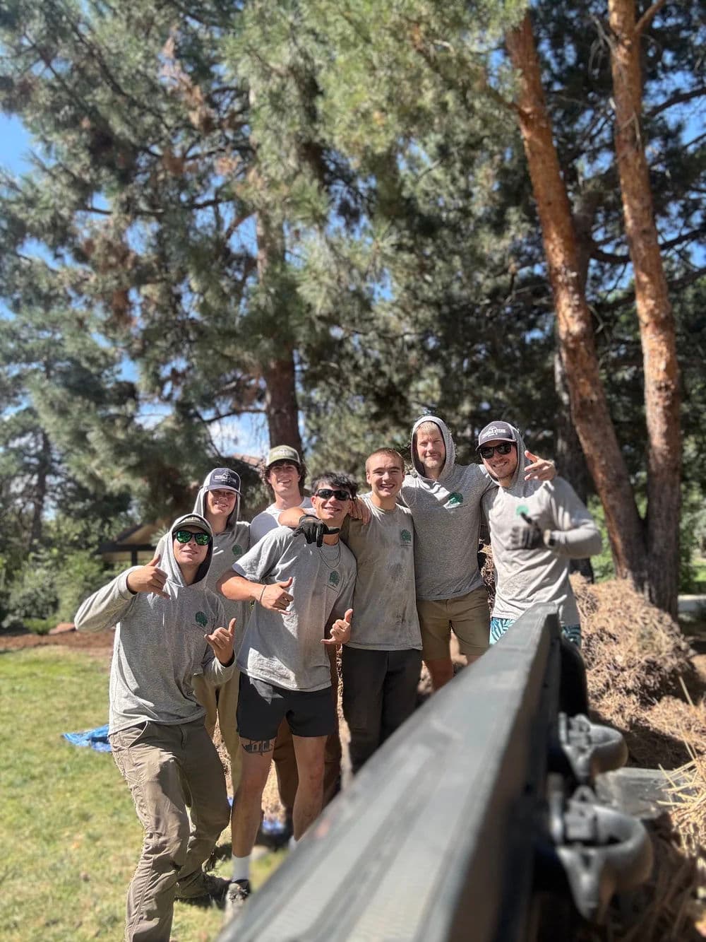 Group of seven smiling volunteers in matching shirts, posing outdoors among tall trees.