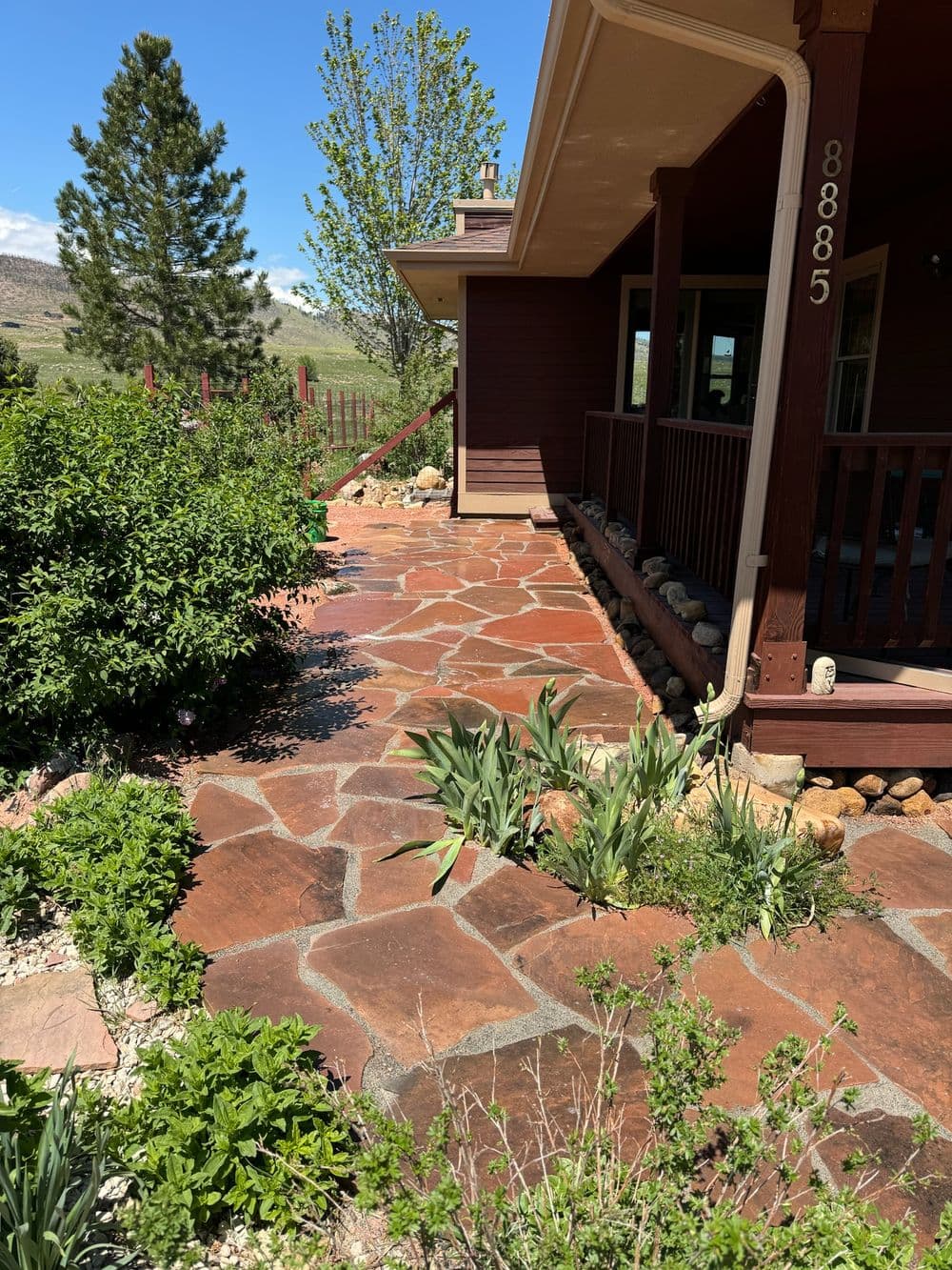 Stone pathway leading to a rustic house surrounded by greenery and scenic hills.