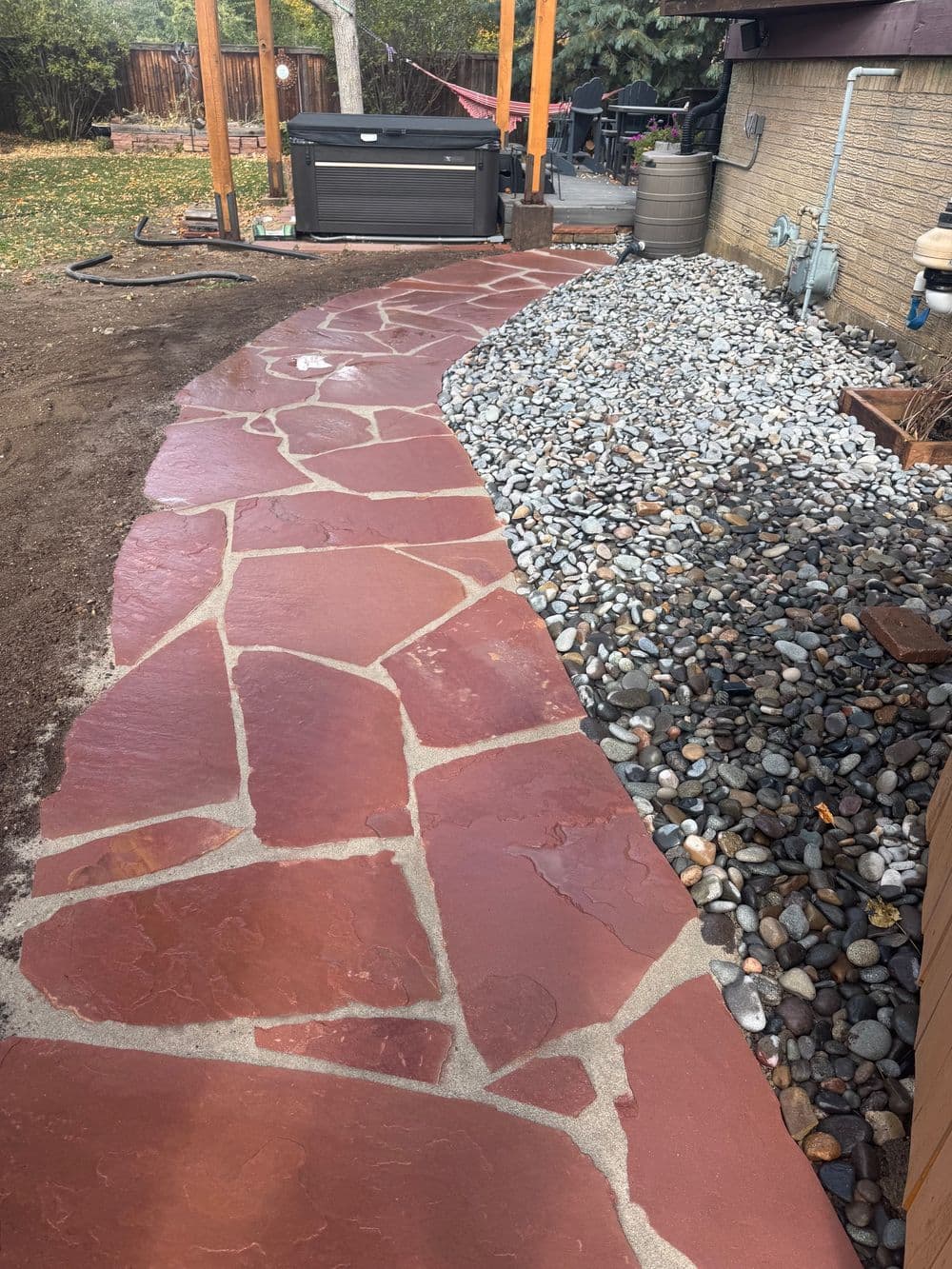Curved stone pathway leading to a gravel area in a backyard landscape.